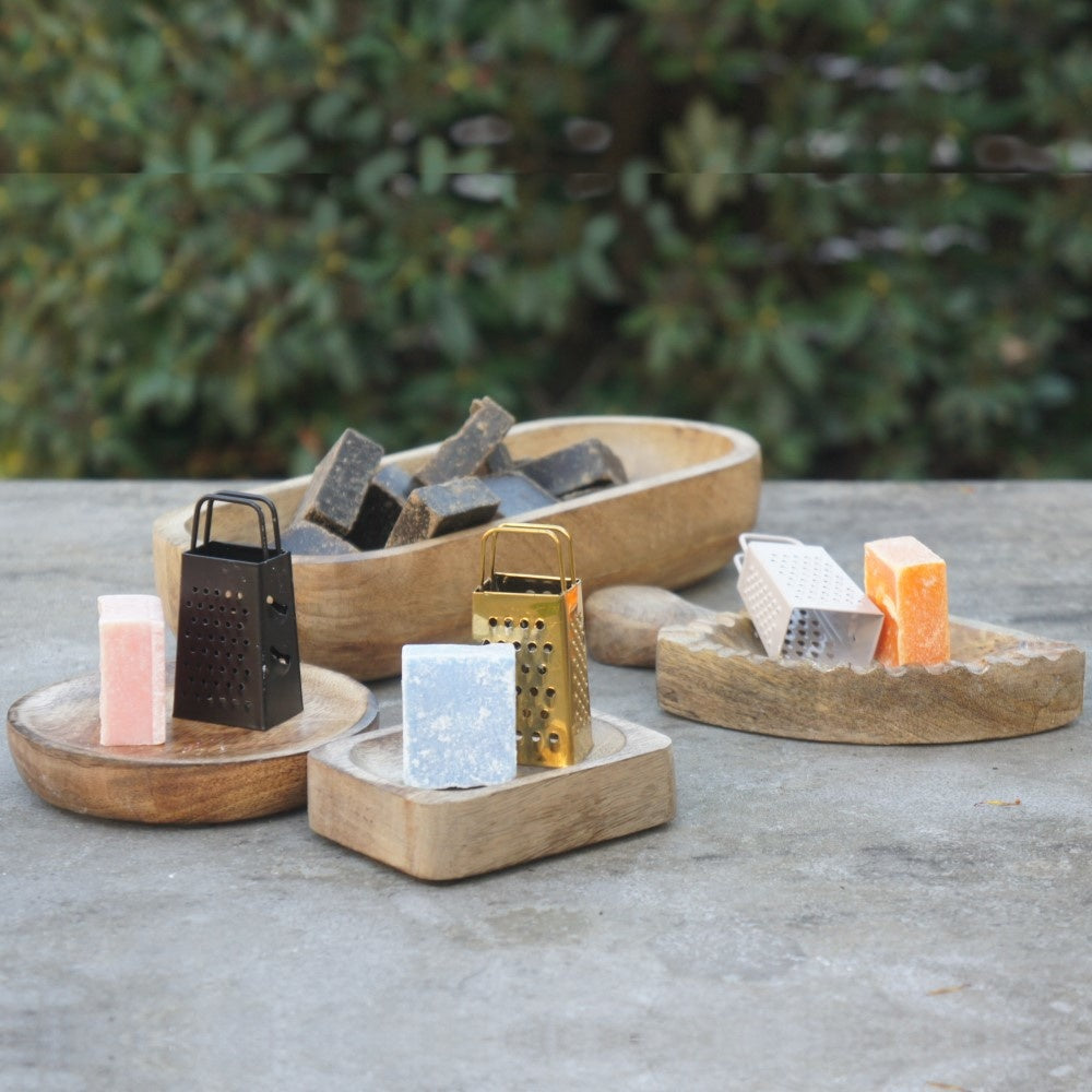 Een sfeervolle setting van diverse mangohouten schaaltjes van Rimisa, gevuld met amberblokjes en gedecoreerd met kleine metalen raspen in zwart, goud en zilver op een rustieke ondergrond.