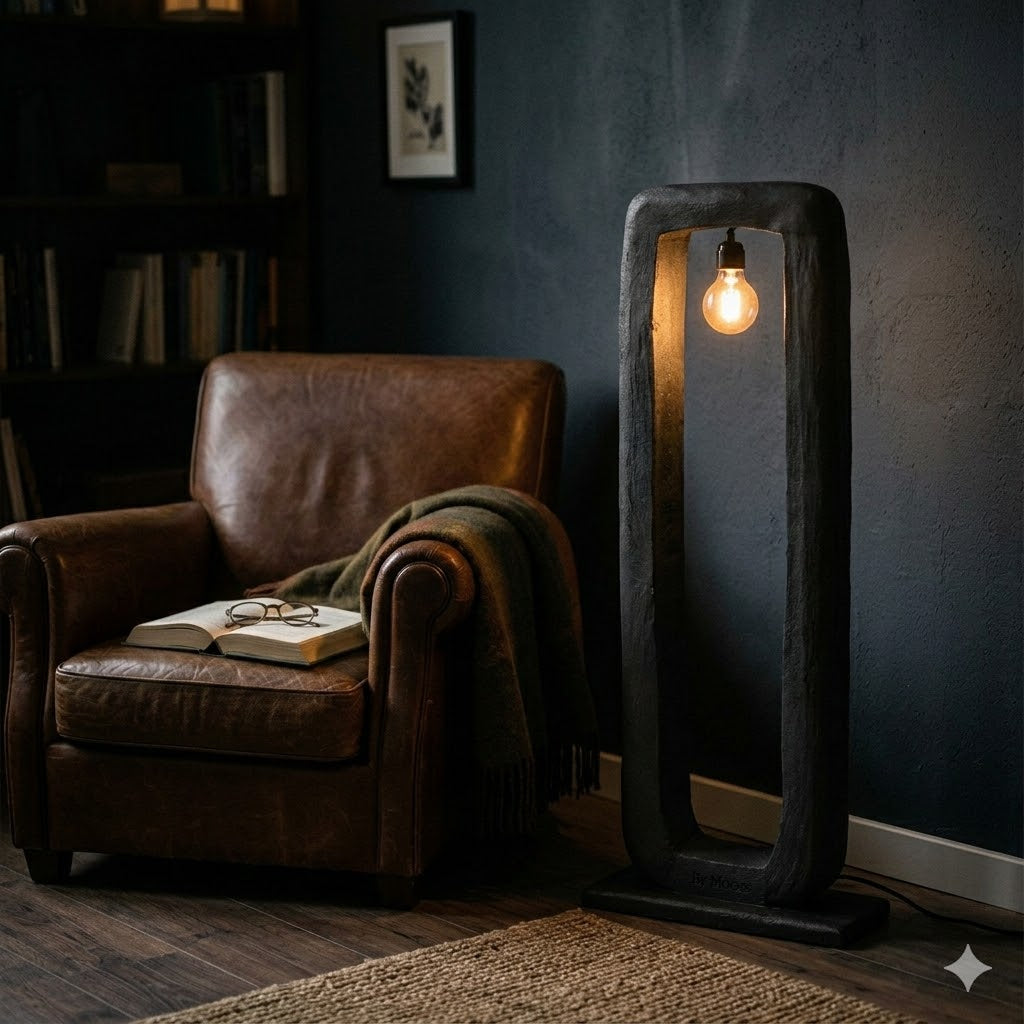 Een sfeervol beeld van de zwart afgewerkte, rechthoekige By Mooss vloerlamp Bali van mango hout, met zijn duidelijk zichtbare voelbare en doorleefde houtstructuur. De lamp staat direct op de grond en verlicht een knusse leeshoek.