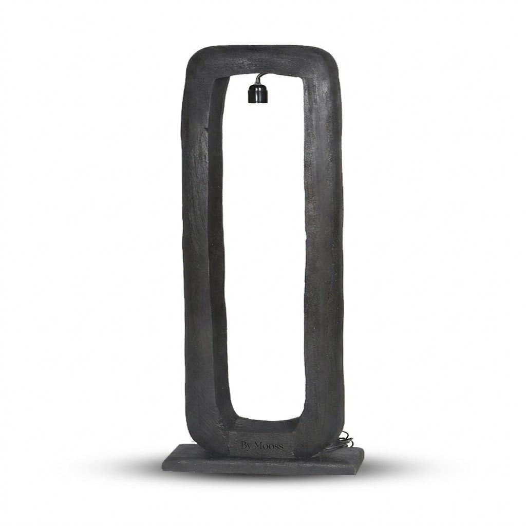 Een eigentijdse By Mooss zwarte vloerlamp Bali, met een rechthoekig mango houten frame en een voelbare houtstructuur, rust op een stabiele, zwarte basis tegen een witte achtergrond. Een zwarte fitting hangt in het frame voor een moderne, industriële uitstraling.