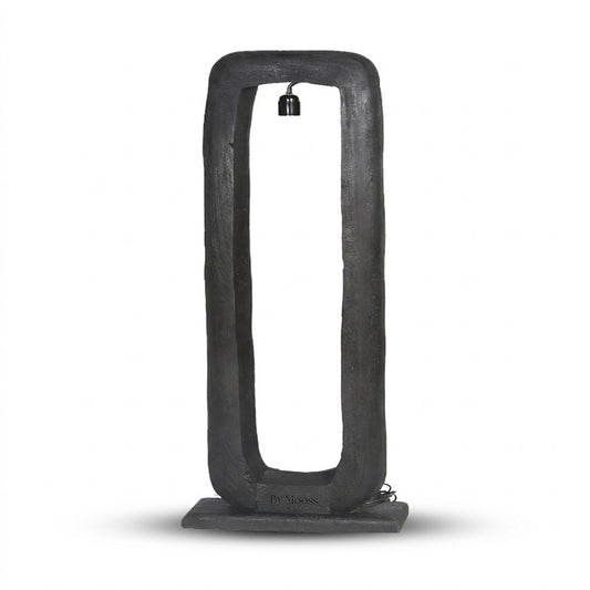 Een eigentijdse By Mooss zwarte vloerlamp Bali, met een rechthoekig mango houten frame en een voelbare houtstructuur, rust op een stabiele, zwarte basis tegen een witte achtergrond. Een zwarte fitting hangt in het frame voor een moderne, industriële uitstraling.