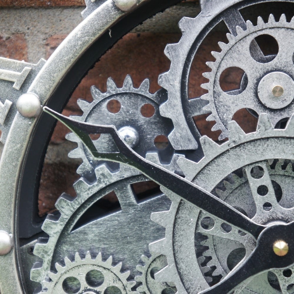 Detailopname van de zwarte wijzers en het mechanische binnenwerk van de zilveren wandklok Nora rimisa.