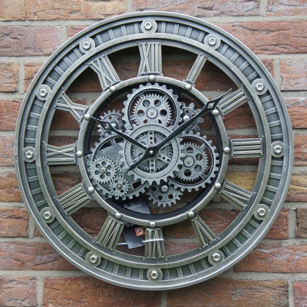 Close-up van de metalen radarklok Nora met Romeinse cijfers hangend aan een rustieke bakstenen wand rimisa.