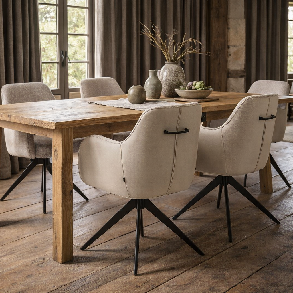 Vier Kyler eetkamerstoelen in beige two-tone stof rond een mangohouten eettafel in een landelijk interieur, met zichtbaar handvat op de rugleuning en zware gordijnen.