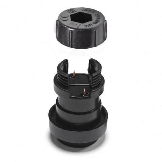 Een gedetailleerde, haarscherpe foto van een zwarte, losse E27 fitting voor prikkabels van Rimisa, getoond in een exploded view. De fitting zelf heeft schroefdraad en koperen prikpinnen, en direct daarboven zweeft de inbusdop met een afdichtring. De technische markeringen zoals IP65 en CE-markering op de inbusdop zijn duidelijk zichtbaar tegen een zuivere witte achtergrond.