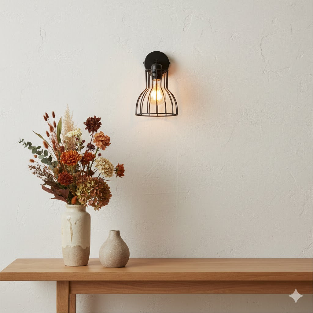 Alt-tekst: Matte zwarte By Moos wandlamp met draadkap gemonteerd boven een eikenhouten wandtafel in Japandi stijl met herfstbloemen en een abstract beeldje.